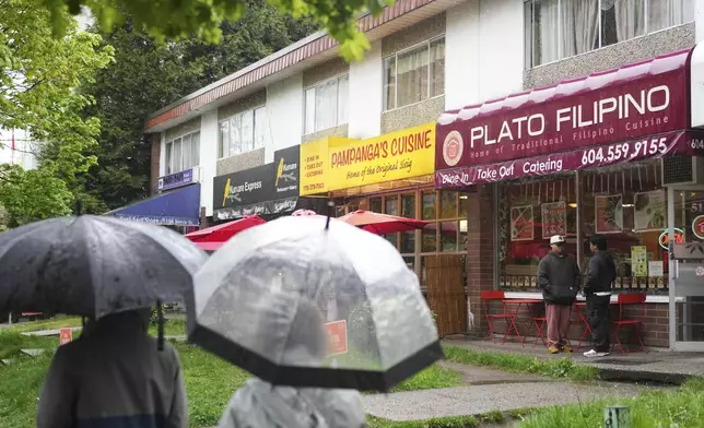 Renzo Javier, second from right, and John Eranzo, right, chat outside Plato Filipino restaurant in Vancouver, British Columbia, Monday, April 28, 2025. (AP Photo/Lindsey Wasson)
