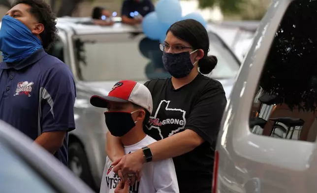 FILE - In this Thursday, May 21, 2020 photo, Vanessa Romero holds her son at a memorial service for the 23rd victim of the Aug. 3 Walmart shooting while wearing an "El Paso Strong" T-shirt and a face mask in El Paso, Texas. AP Photo/Cedar Attanasio, File)