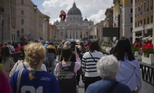 People walk along Via della Conciliazione avenue to line up to view Pope Francis lying in state inside St. Peter's Basilica, seen in the background, at the Vatican, Thursday, April 24, 2025. (AP Photo/Andrew Medichini)