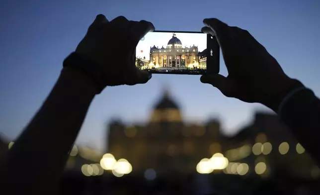 A man takes a picture of St. Peter's Basilica as faithful gather in St. Peter's Square at the Vatican, Wednesday, April 23, 2025 as the body of the late Pope Francis will lie in state inside St. Peter's Basilica for three days. (AP Photo/Markus Schreiber)