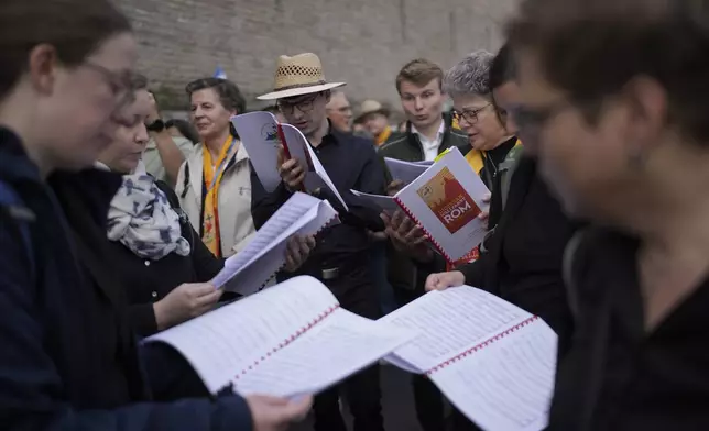 People look at booklets as they wait in line to view Pope Francis lying in state inside St. Peter's Basilica, at the Vatican, Thursday, April 24, 2025. (AP Photo/Markus Schreiber)