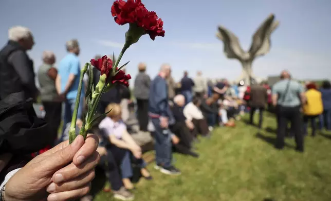 A person holds a flower as people gather around the monument commemorating victims of a World War II concentration camp, where tens of thousands of people perished in the hands of the pro-Nazi puppet regime at the time, in Jasenovac, Croatia, Tuesday, April 22, 2025. (AP Photo)