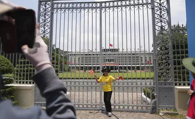 A woman holding Vietnamese flags stands in front of the Independence Palace in Ho Chi Minh City, Vietnam Tuesday, April 29, 2025. (AP Photo/Hau Dinh)