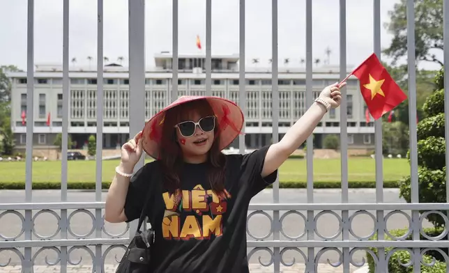 A woman waves a Vietnamese flag in front of the Independence Palace in Ho Chi Minh City, Vietnam Tuesday, April 29, 2025. (AP Photo/Hau Dinh)