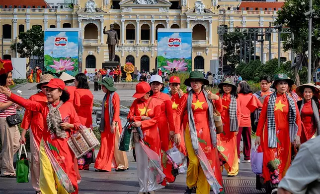 Vietnamese women in traditional dress with a motif of a Vietnamese flag walk past Ho Chi Minh City Hall, on Tuesday, April 29, 2025 ahead of the 50th anniversary of the end of the Vietnamese War. (AP Photo/Richard Vogel)