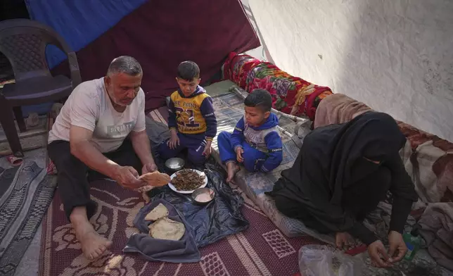 Members of the Al-Basyouni family, displaced from Beit Hanoun, eat in their tent at the Islamic University in Gaza City, which now is a shelter for displaced Palestinians amid the ongoing war in Gaza, Friday, April 4, 2025. (AP Photo/Jehad Alshrafi)