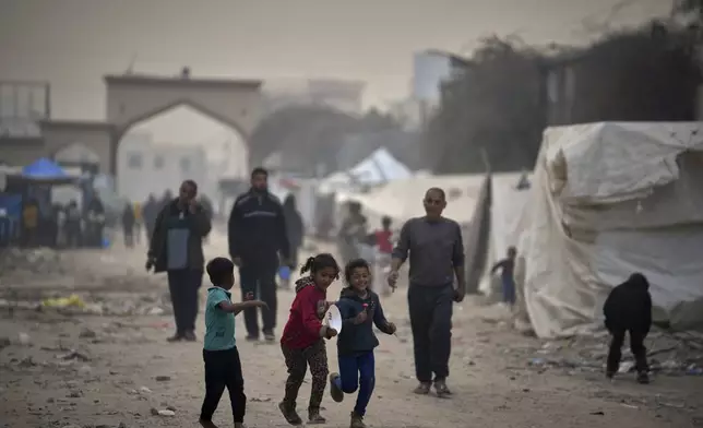 Displaced Palestinians walk by tents at the Islamic University of Gaza compound amid the ongoing war in Gaza, Sunday, April 6, 2025. (AP Photo/Jehad Alshrafi)
