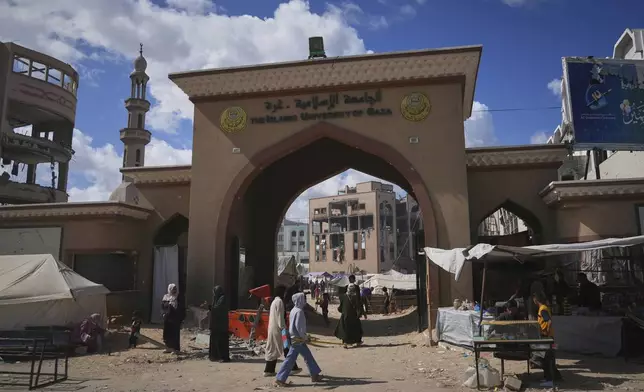 Palestinians walk by the gate of the Islamic University in Gaza City, which now is a shelter for displaced Palestinians amid the ongoing war in Gaza, Saturday, April 5, 2025. (AP Photo/Jehad Alshrafi)