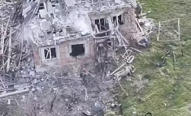 This image taken from video that European military officials say was filmed by a Ukrainian drone in the southern Ukrainian village of Piatykhatky on March 13, 2025, shows a soldier, left, identified as Russian, pointing his gun at a Ukrainian soldier who appears to be surrendering after emerging from the ruins of a house to join other Ukrainian prisoners on the ground. (Ukraine Military/European Defense Officials via AP)