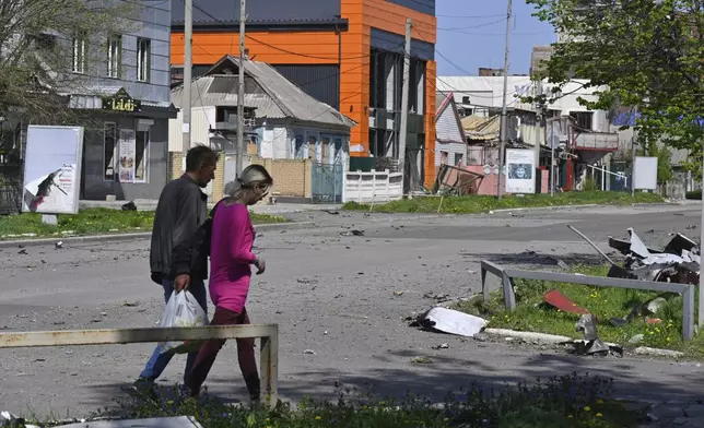 Local residents walk past damaged buildings in central Pokrovsk, the site of the heaviest battles with the Russian troops in the Donetsk region, Ukraine, Wednesday, April 23, 2025. (AP Photo/Michael Shtekel)