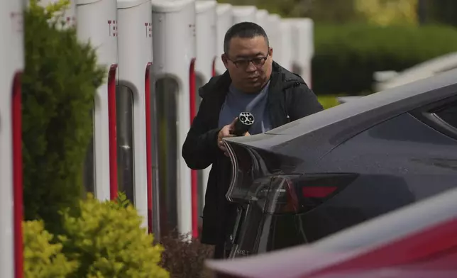 A man gets his Tesla vehicle charged at an electric vehicle charging station outside of a Tesla dealership, in Beijing, Wednesday, April 9, 2025. (AP Photo/Andy Wong)