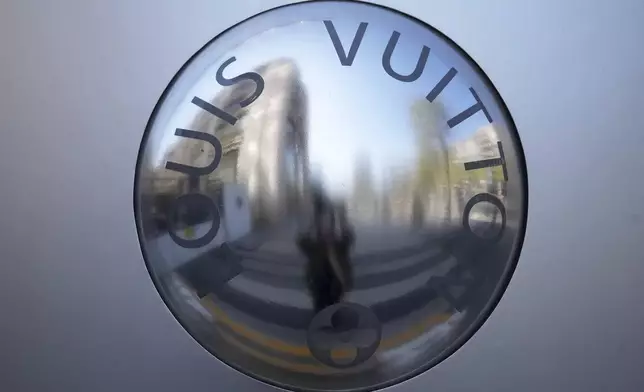 A person is reflected in a decoration of the Louis Vuitton flagship store Wednesday, April 9, 2025 in Paris. (AP Photo/Michel Euler)