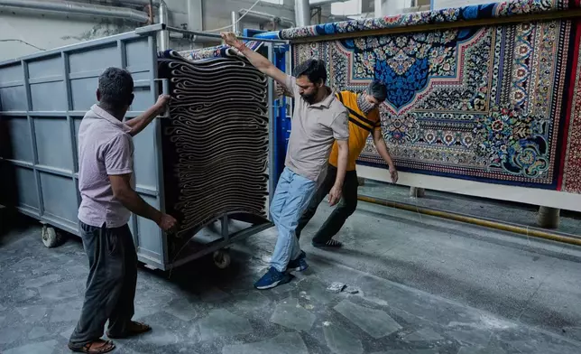 Indian workers push a cart loaded with carpets at a factory on the outskirts of Jammu, India, Tuesday, April 8, 2025. (AP Photo/Channi Anand)
