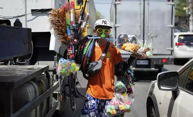 Filipino Andy Chavez peddles different kinds of goods to motorists during traffic along a busy street in Quezon city, Philippines, Thursday, April 10, 2025. (AP Photo/Aaron Favila)