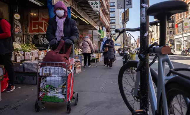 A person with a shopping bag and cart walks past a grocery store in the Chinatown neighborhood, Wednesday, April 9, 2025, in New York. (AP Photo/Yuki Iwamura)