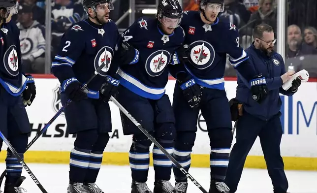 Winnipeg Jets' Dylan Samberg (54) is helped off the ice by Dylan Demelo (2) and Morgan Barron (36) after blocking an Edmonton Oilers shot during second period NHL action in Winnipeg, Sunday April 13 2025. (Fred Greenslade/The Canadian Press via AP)