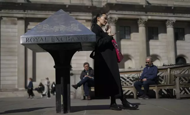 A woman holds her phone as she stands outside the Bank of England in the financial district known as The City, in London, Wednesday, April 9, 2025. (AP Photo/Alberto Pezzali)