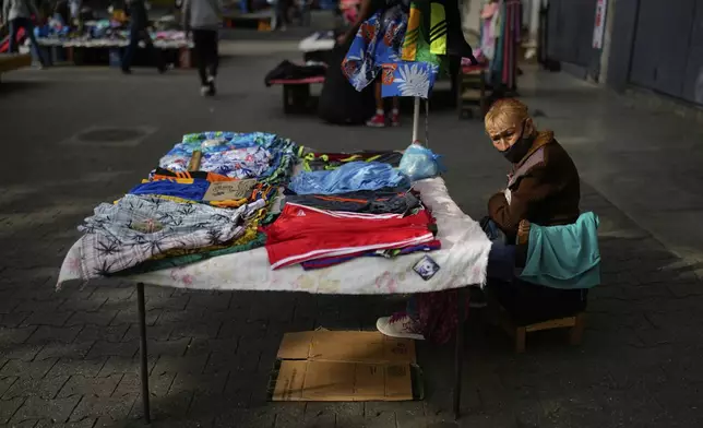 A clothing vender sits at her table on the sidewalk in Caracas, Venezuela, Friday, April 11, 2025. (AP Photo/Ariana Cubillos)
