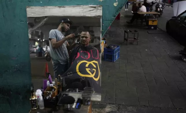John Rodriguez cuts a client's hair under the Fuerzas Armadas bridge in Caracas, Venezuela, Thursday, April 10, 2025. (AP Photo/Ariana Cubillos)
