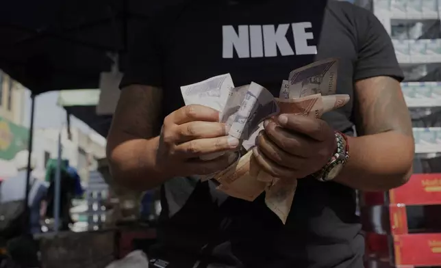 A man counts Venezuelan Bolivars at a street market in Caracas, Venezuela, Friday, April 11, 2025. (AP Photo/Ariana Cubillos)