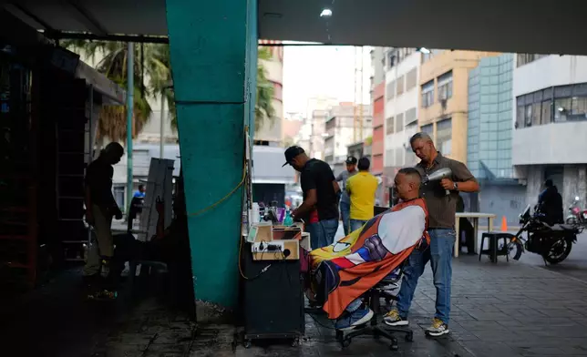 A man gets a haircut under the Fuerzas Armadas bridge in Caracas, Venezuela, Thursday, April 10, 2025. (AP Photo/Ariana Cubillos)