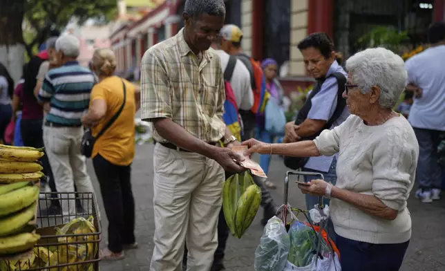 Arnold Guerrero, left, sells plantains to a pedestrian in Caracas, Venezuela, Friday, April 11, 2025. (AP Photo/Ariana Cubillos)