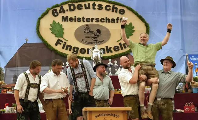 Competitors celebrates after their bouts while they try to pull the opponents over the table at the German Championships in Fingerhakeln or finger wrestling, in Pang, near Rosenheim, Germany, Sunday, April 27, 2025. (AP Photo/Matthias Schrader)