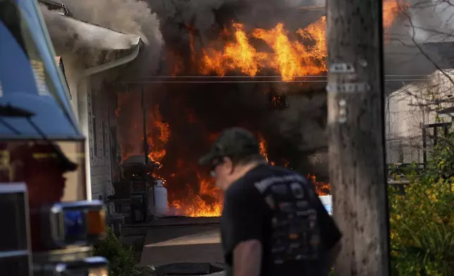 A man walks past a house fire Wednesday, April 23, 2025, in Lacey Township, N.J. (AP Photo/Matt Slocum)
