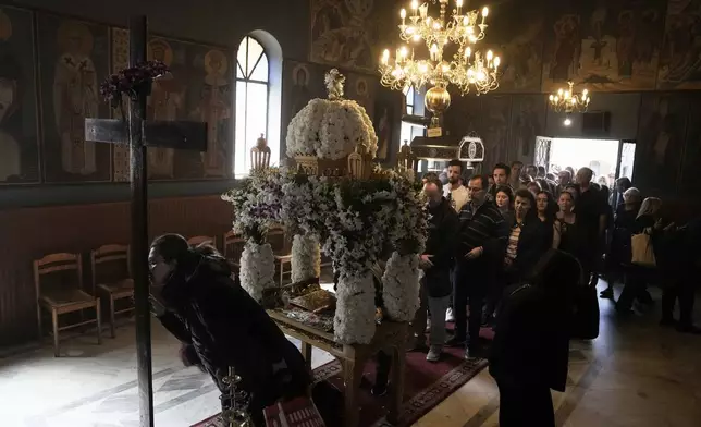 A woman kisses a crucifix as others wait behind the "Epitaph," after the procession of Jesus' funeral bier, at Agioi Taxiarches church cemetery in Chalandri cemetery, in northern Athens, Greece, Friday, April 18, 2025. (AP Photo/Thanassis Stavrakis)