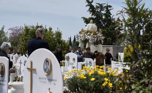 The procession of Jesus' funeral bier, known as the "Epitaph" in Greek, pass next to graves at a cemetery in Chalandri suburb, in northern Athens, Greece, Friday, April 18, 2025. (AP Photo/Thanassis Stavrakis)