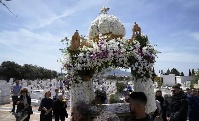 The procession of Jesus' funeral bier, known as the "Epitaph" in Greek, pass next to graves at a cemetery in Chalandri suburb, in northern Athens, Greece, Friday, April 18, 2025. (AP Photo/Thanassis Stavrakis)