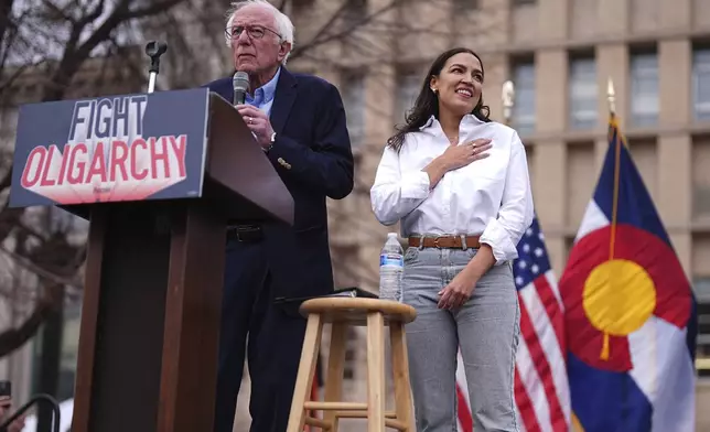 Sen. Bernie Sanders, I-Vt., left, speaks as Rep. Alexandria Ocasio-Cortez, D-N.Y., responds to calls of support during a stop of their "Fighting Oligarchy" tour that filled Civic Center Park, Friday, March 21, 2025, in Denver. (AP Photo/David Zalubowski)