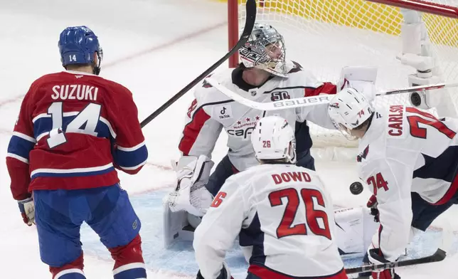 Montreal Canadiens' Nick Suzuki (14) scores against Washington Capitals goaltender Logan Thompson, center top, during the second period of Game 3 of a first-round NHL hockey playoff series in Montreal, Friday, April 25, 2025. (Christinne Muschi/The Canadian Press via AP)