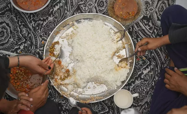 The Al-Najjar family eats peas with rice in their family tent in Muwasi, on the outskirts of Khan Younis in the southern Gaza Strip, Friday, April, 25, 2025.(AP Photo/Abdel Kareem Hana)