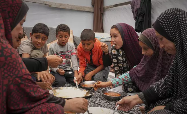 The Al-Najjar family eats peas with rice in their family tent in Muwasi, on the outskirts of Khan Younis in the southern Gaza Strip, Friday, April, 25, 2025. (AP Photo/Abdel Kareem Hana)