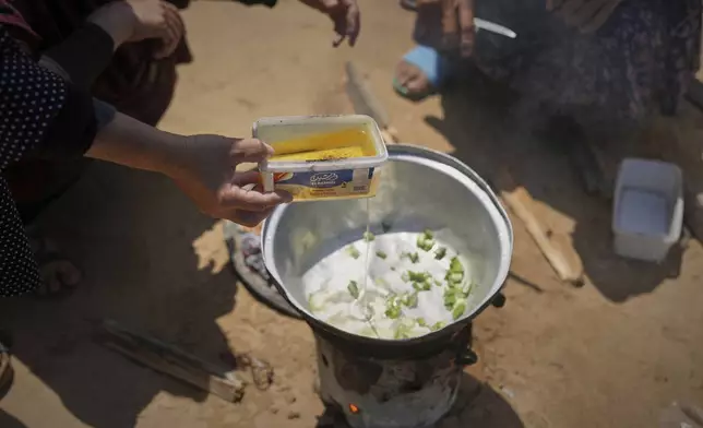 Somaya Al-Najjar, 60, pours frying oil to cook peas in their family tent in Muwasi, on the outskirts of Khan Younis in the southern Gaza Strip, Friday, April 25, 2025. (AP Photo/Abdel Kareem Hana)