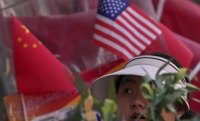 A woman walks past Chinese and United States' national flags on display at a merchandise store in Beijing, Thursday, April 3, 2025. (AP Photo/Andy Wong)