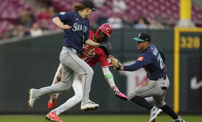 Cincinnati Reds' Elly De La Cruz, center, is tagged out trying to steal third base by Seattle Mariners second baseman Dylan Moore, right, after taking the throw from pitcher Bryce Miller, left, in the fourth inning of a baseball game, Wednesday, April 16, 2025, in Cincinnati. (AP Photo/Carolyn Kaster)
