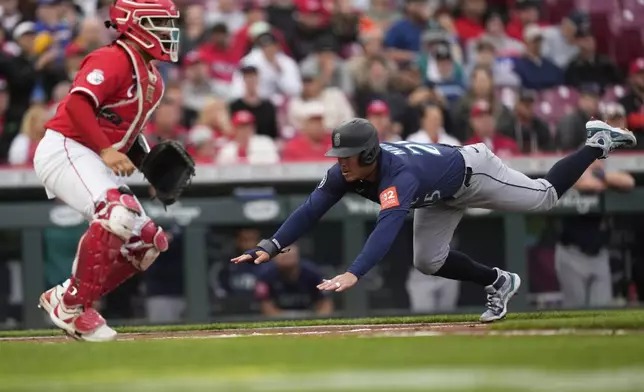 Seattle Mariners' Dylan Moore dives into home plate to score on a single hit by Ben Williamson as Cincinnati Reds catcher Jose Trevino, right, waits for the throw in the second inning of a baseball game, Wednesday, April 16, 2025, in Cincinnati. (AP Photo/Carolyn Kaster)