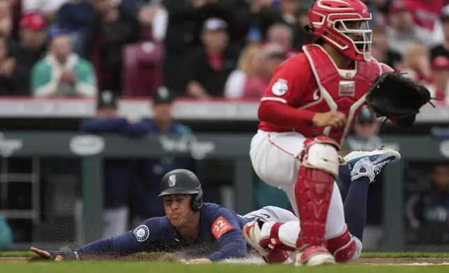 Seattle Mariners' Dylan Moore slides across home plate to score on a single hit by Ben Williamson as Cincinnati Reds catcher Jose Trevino, right, waits for the throw in the second inning of a baseball game, Wednesday, April 16, 2025, in Cincinnati. (AP Photo/Carolyn Kaster)