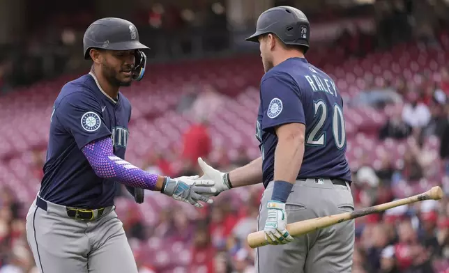 Seattle Mariners' Julio Rodríguez, left, celebrates with Seattle Mariners Luke Raley, right, after scoring on a double hit by Randy Arozarena in the first inning of a baseball game against the Cincinnati Reds, Wednesday, April 16, 2025, in Cincinnati. (AP Photo/Carolyn Kaster)
