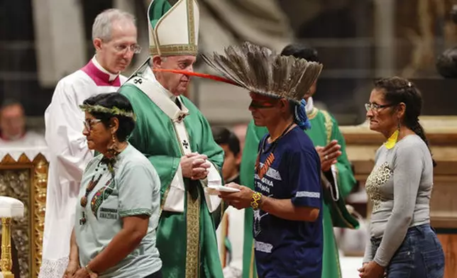 FILE - Indigenous peoples, some with their faces painted and wearing feathered headdresses, walk past Pope Francis as he celebrates an opening Mass for the Amazon synod, in St. Peter's Basilica, at the Vatican, Sunday, Oct. 6, 2019. (AP Photo/Andrew Medichini, file)