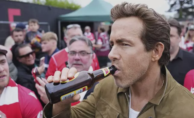 Wrexham co-owner Ryan Reynolds sips beer prior to the English League One soccer match between Wrexham and Charlton Athletic at the Racecourse ground in Wrexham, Wales, Saturday, April 26, 2025. (AP Photo/Jon Super)