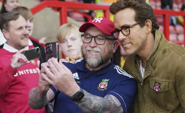 Wrexham co-owners Ryan Reynolds, right, poses with fans before the English League One soccer match between Wrexham and Charlton Athletic at the Racecourse ground in Wrexham, Wales, Saturday, April 26, 2025. (AP Photo/Jon Super)