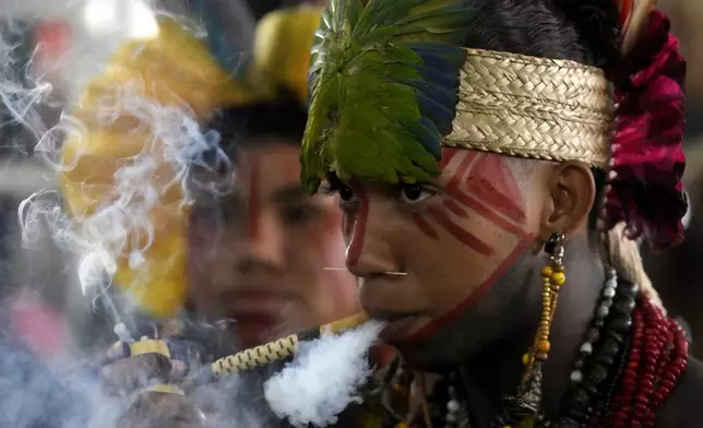 A Pataxso Indigenous youth smokes a traditional pipe during the Free Earth camp held annually to demand more government attention to Indigenous issues in Brasilia, Brazil, Monday, April 7, 2025. (AP Photo/Eraldo Peres)