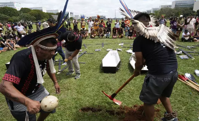 Indigenous people dig a hole for an empty coffin, symbolizing the death of lawmakers who they say are against their rights and territorial protection, during a march at the annual Free Earth camp in Brasilia, Brazil, Tuesday, April 8, 2025. (AP Photo/Eraldo Peres)