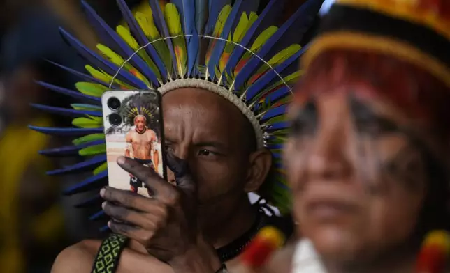 An Indigenous man takes photos with his cell phone during the Free Earth camp held annually to demand more government attention to Indigenous issues in Brasilia, Brazil, Monday, April 7, 2025. (AP Photo/Eraldo Peres)