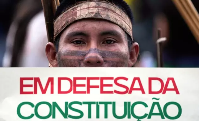 An Indigenous man holds a sign that reads in Portuguese: "In defense of the Constitution" during the march coined: "We are the answer" in Brasilia, Brazil, Thursday, April 10, 2025, during the annual Free Earth camp where Brazil's Indigenous people discuss rights, territorial protection and their role in COP30 which will take place for the first time in the Amazon. (AP Photo/Eraldo Peres)