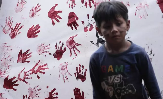 An Indigenous boy stands next to a banner covered in red-ink hand prints during the "We are the answer" march during the annual Free Earth camp, where they discuss rights, territorial protection and their role in COP30, which will take place for the first time in the Amazon, in Brasilia, Brazil, Thursday, April 10, 2025. (AP Photo/Eraldo Peres)