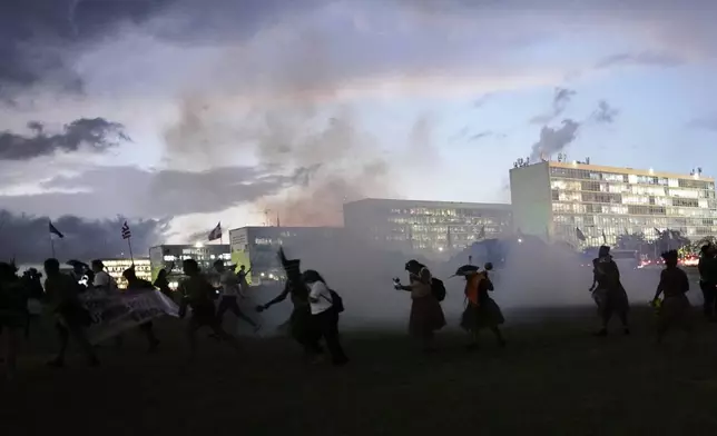 Indigenous people run away from tear gas fired by the police, after trying to enter Congress during the "We are the answer" march at the annual Free Earth camp, where they discuss rights, territorial protection and their role in COP30, which will take place in the Amazon, in Brasilia, Brazil, Thursday, April 10, 2025. (AP Photo/Eraldo Peres)